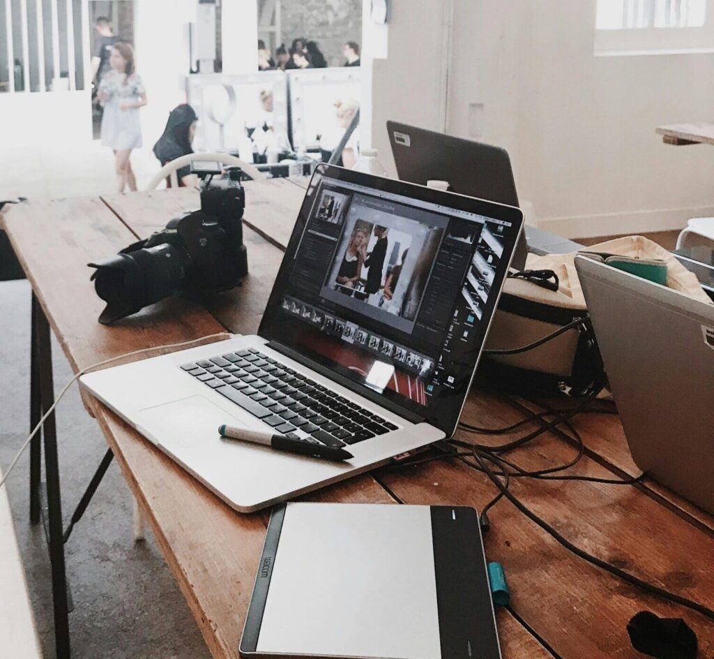 A bright, modern workspace featuring laptops, a camera, and a drawing tablet in an indoor office.